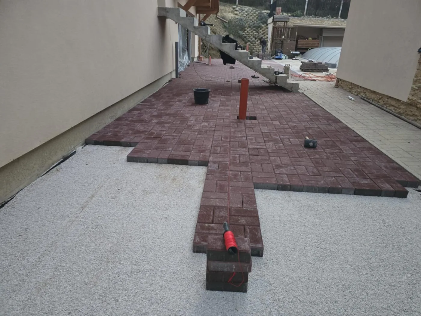 Vörös téglakő parketta-kötésben ház mellett, zúzottkő ágyazaton, lerakás közben